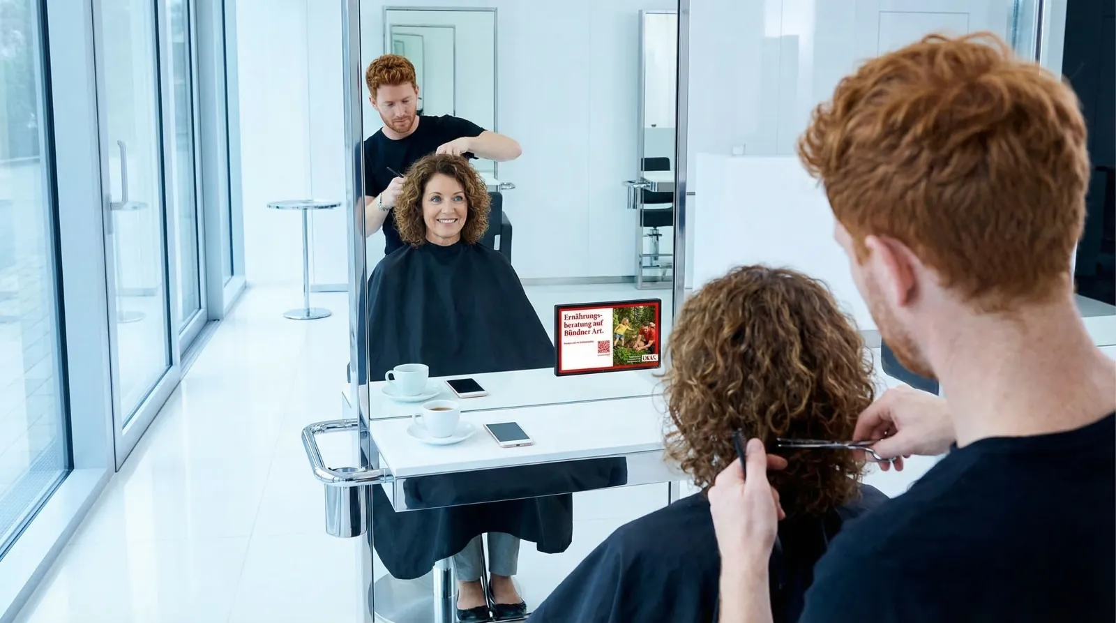 Frau, 50 im Salon und im Studio, auf dem Screen die Werbung von ÖKK