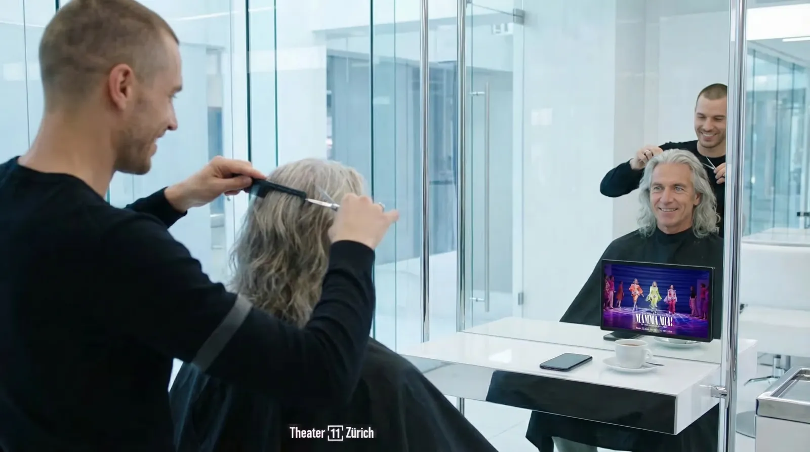 Mann, 60 im Coiffeursalon, auf dem Screen der Spot von Rent a Show (Mamma Mia)