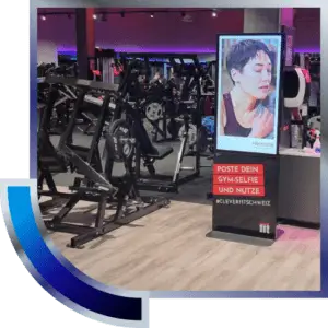 Digitale DOOH-Werbung im Fitnessstudio neben Trainingsgeräten und Tresen